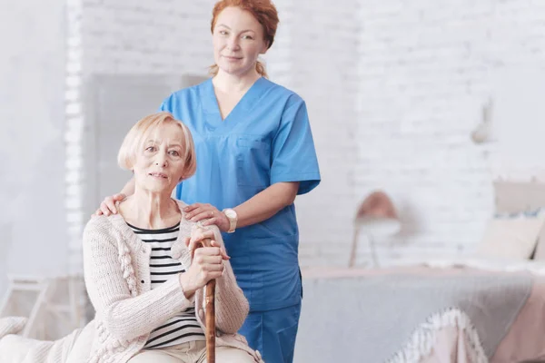 Cuidadora femenina consciente de pie junto a su paciente mayor — Foto de Stock