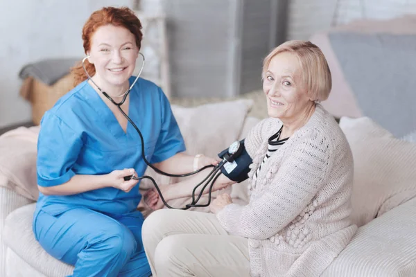 La señora mayor y su enfermera sonriendo mientras miden la presión — Foto de Stock