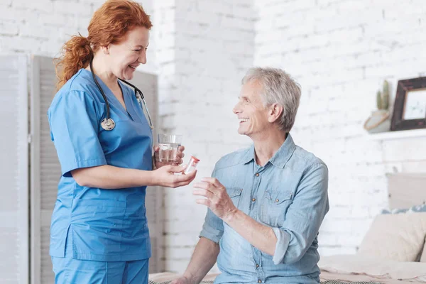 Stralende verzorger pekelen pillen voor vrolijke senior man — Stockfoto