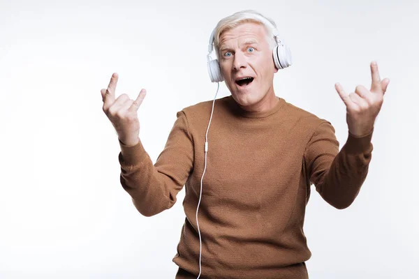 Homme âgé écoutant de la musique et montrant un signe de cornes — Photo