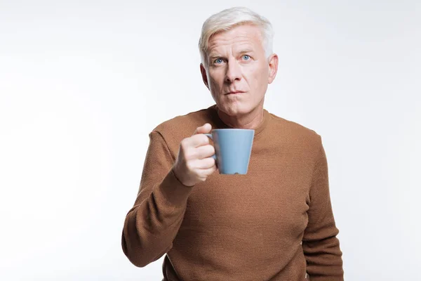 Senior hält Tasse Kaffee in der Hand und runzelt die Stirn — Stockfoto