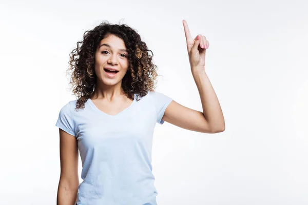 Mujer rizada en camiseta blanca apuntando hacia arriba con el dedo — Foto de Stock