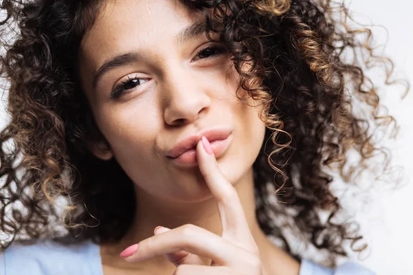 Curly-haired woman pouting and pressing finger to lips — Stock Photo, Image