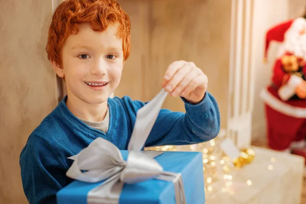 Очаровательный ребенок улыбается в камеру, открывая подарок. — стоковое фото