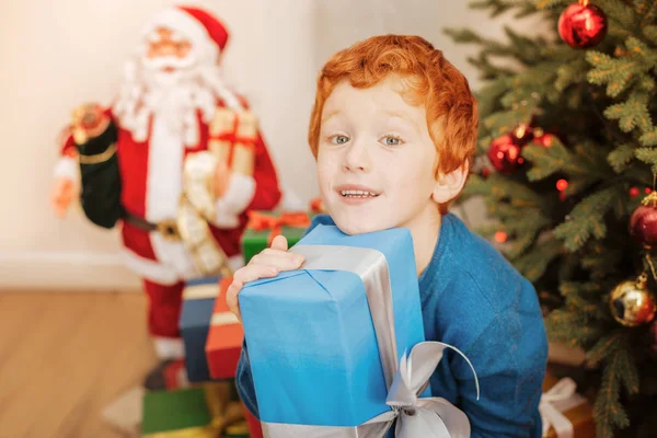 Милый рыжий мальчик крепко обнимает рождественский подарок — стоковое фото
