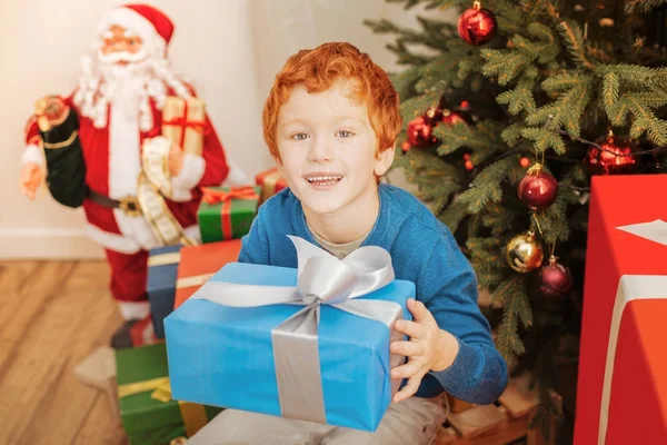 Возбужденный рыжий ребенок улыбается, держа в руках рождественский подарок — стоковое фото