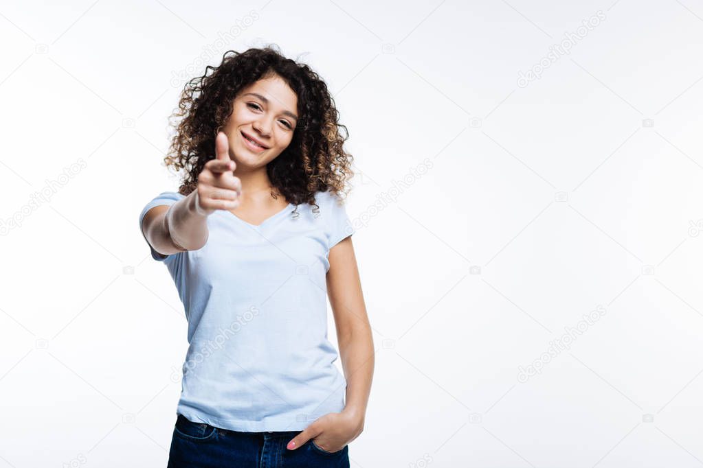 Cheerful curly woman pointing at the camera with finger
