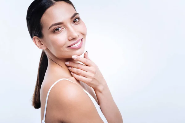 Cheerful dark-haired woman smiling while touching her chin — Stock Photo, Image