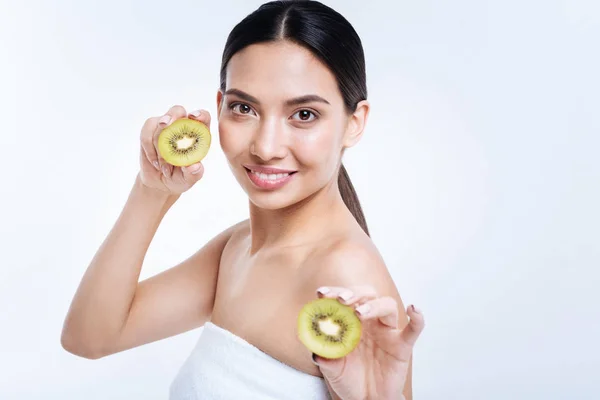 Leende kvinna poserar med två halvor av kiwifrukt — Stockfoto