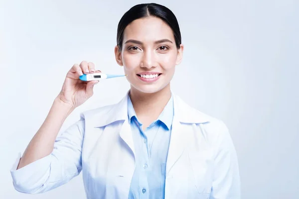 Optymistyczne lekarka trzyma termometr i uśmiechając się — Zdjęcie stockowe