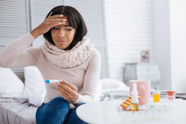 Mujer molesta con alta temperatura mirando los medicamentos — Foto de Stock