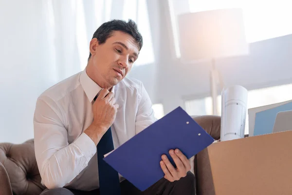 Jovem irritado sentado com uma prancheta azul depois de perder o emprego — Fotografia de Stock