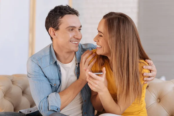 Femme souriante émotionnelle tenant un smartphone tout en étant assis avec son homme bien-aimé — Photo