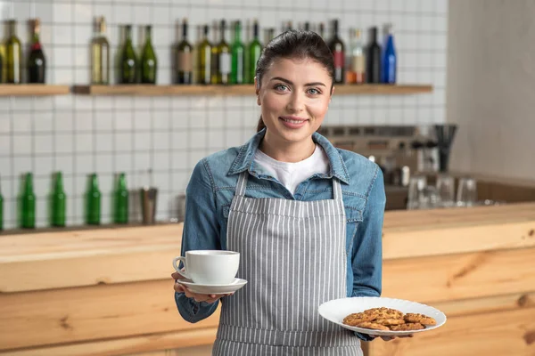 Adorable young waitress holding a cup of coffee and tasty biscuits — Stock Photo, Image