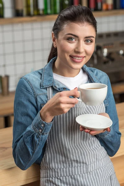 Hermosa camarera sonriente bebiendo té mientras tiene tiempo libre en el trabajo — Foto de Stock