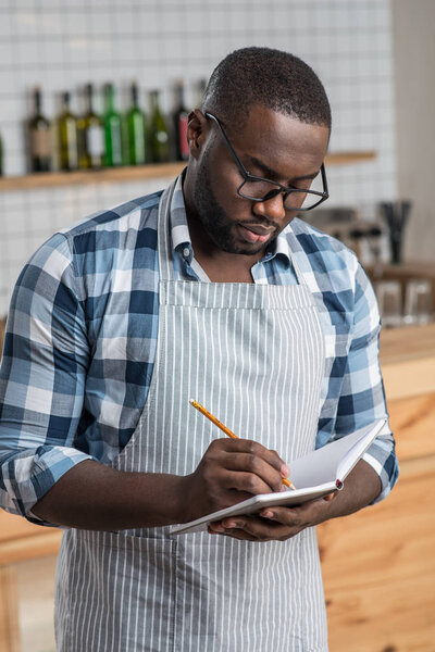 Attentive worker of a cafe standing and making important notes