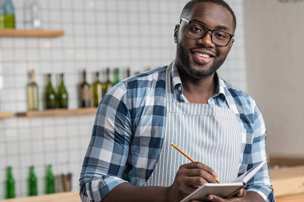 Smiling positive waiter standing with a notebook and writing