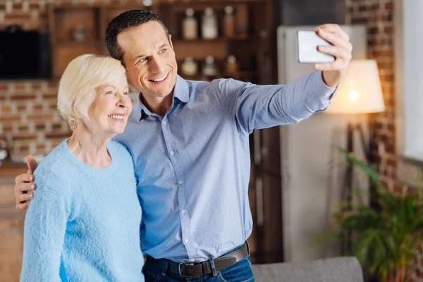 Szczęśliwy młody człowiek i jego matka starszy biorąc selfie — Zdjęcie stockowe