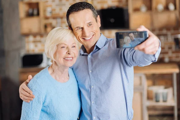 Piękny podeszłym wieku kobieta i jej syn robienia selfie w kuchni — Zdjęcie stockowe
