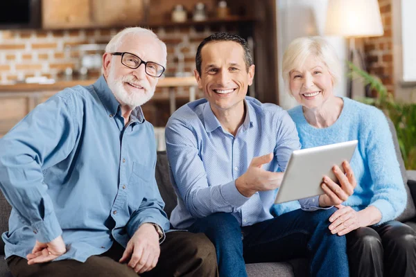 Mladý muž a jeho staré rodiče pózuje při používání tabletu — Stock fotografie