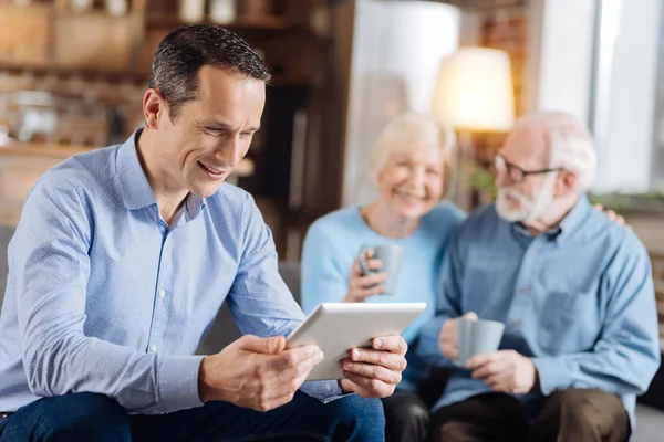 Pleasant man reading from tablet while his parents talking — Stock Photo, Image