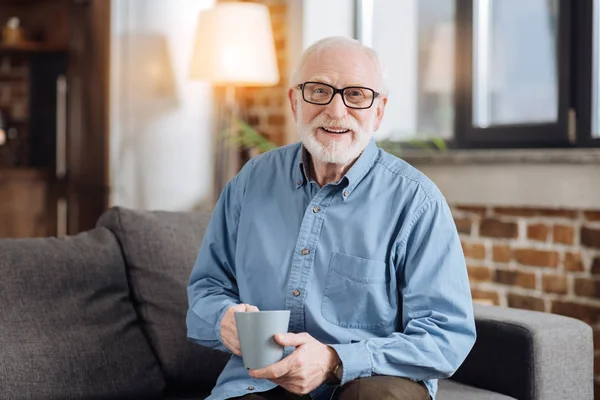 Anciano posando con una taza de café en el sofá — Foto de Stock