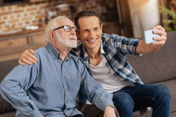 Hombre optimista tomando una selfie con su padre anciano —  Fotos de Stock