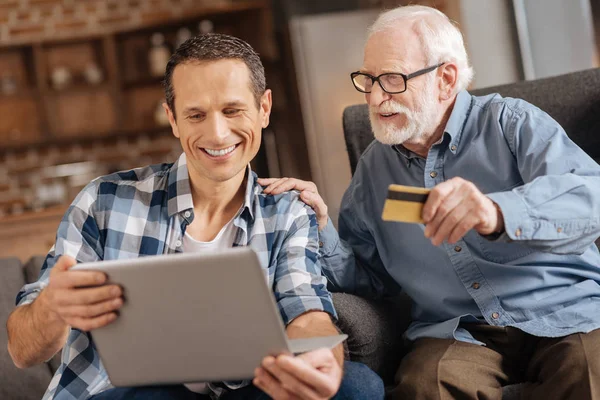 Пожилой человек дает банковскую карточку сыну, делающему покупки в интернете — стоковое фото