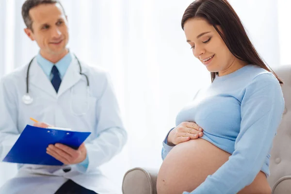 Positiv brunett tittar på hennes stora mage — Stockfoto