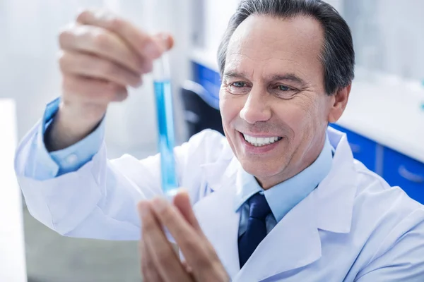 Cheerful positive man looking at the test tube — Stock Photo, Image