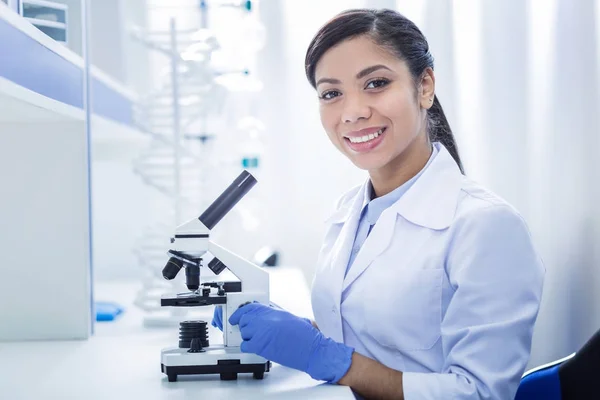 Delighted smart woman sitting in front of the microscope — Stock Photo, Image