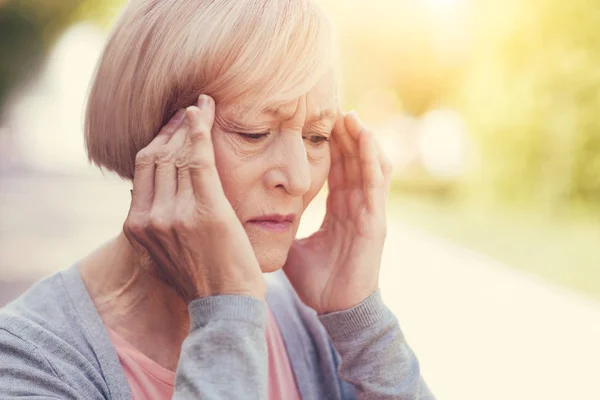 Cheerless elderly woman holding her temples — Stock Photo, Image