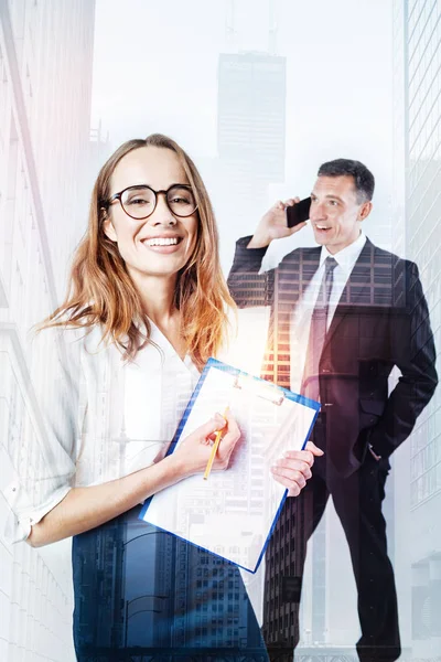 Homem com um telefone atrás de uma mulher sorridente com uma pasta — Fotografia de Stock