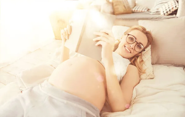 Положительная беременная женщина читает книгу в постели — стоковое фото