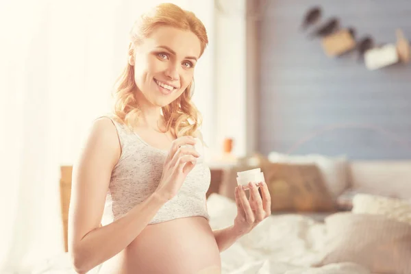 Красивая улыбающаяся беременная женщина с косметическим продуктом — стоковое фото