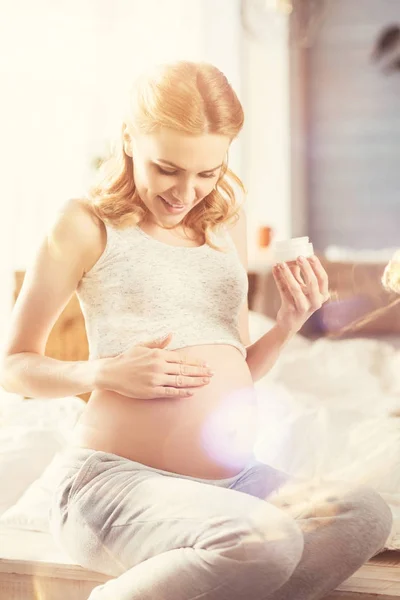 Positive pregnant woman applying body cream — Stock Photo, Image