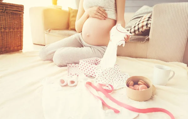 Angenehme schwangere Frau mit Babykleidung — Stockfoto