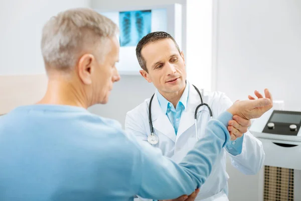 Smart professional therapist looking at the patients hand — Stock Photo, Image