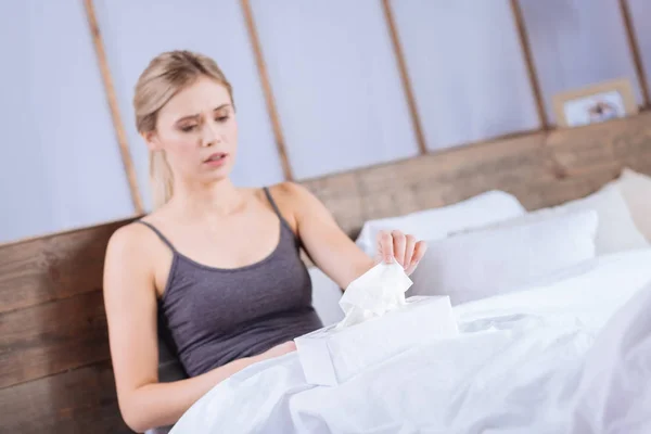 Ill young woman lying in the bed and taking a tissue — Stock Photo, Image