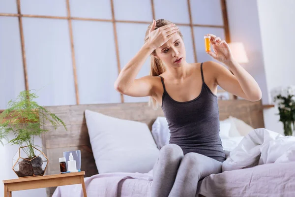 Wanita muda sakit dengan demam melihat pil kontainer — Stok Foto