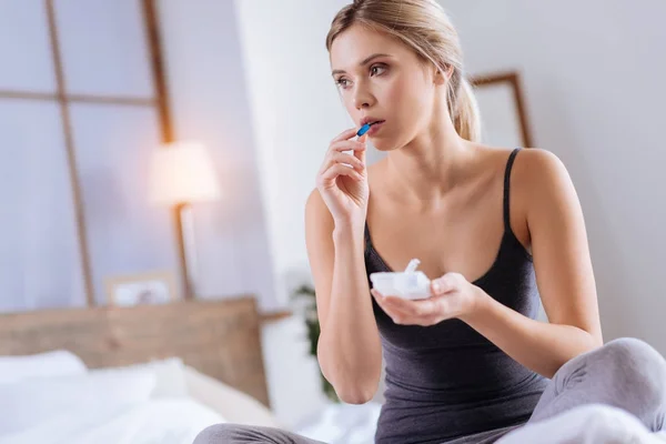 Mujer de cabello rubio tomando una cápsula azul mientras está sentada en la cama — Foto de Stock