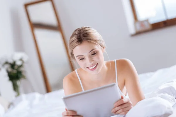 Cheerful young woman reading from tablet in bed