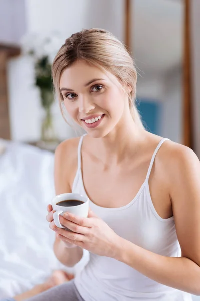 Mujer alegre posando con una taza de café en el dormitorio — Foto de Stock