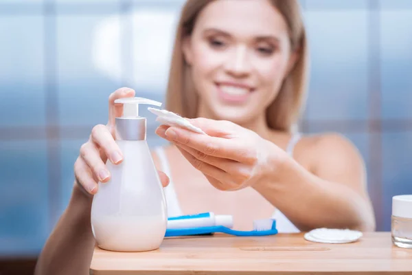 Femme souriante mettant un produit de soins de la peau sur un coton — Photo