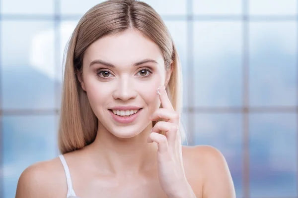 Beautiful young woman applying cream to her face — Stock Photo, Image