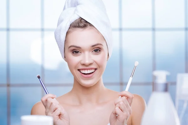 Счастливая молодая женщина позирует с двумя кисточками для макияжа — стоковое фото