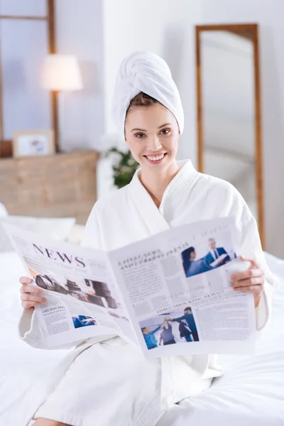 Vrolijke vrouw zittend op bed en het lezen van de krant — Stockfoto
