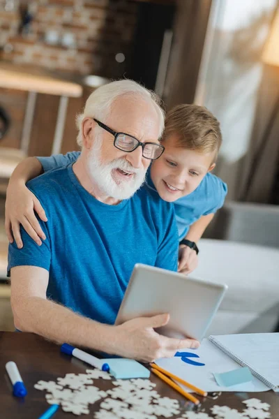 Веселый позитивный мальчик стоит позади своего дедушки — стоковое фото