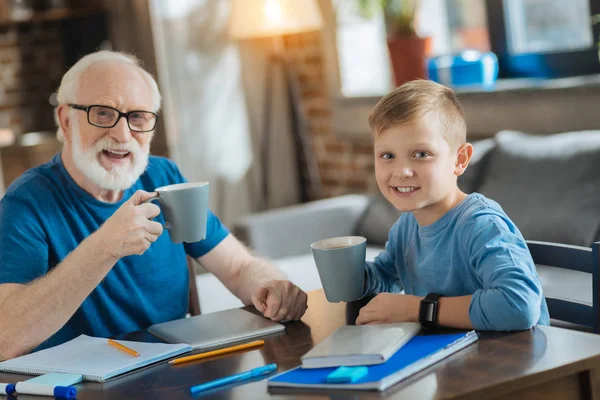 Счастливый позитивный мальчик пьет чай со своим дедушкой — стоковое фото