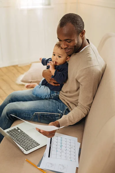 Lachende vader werken op de laptop en het bedrijf van zijn zoon — Stockfoto